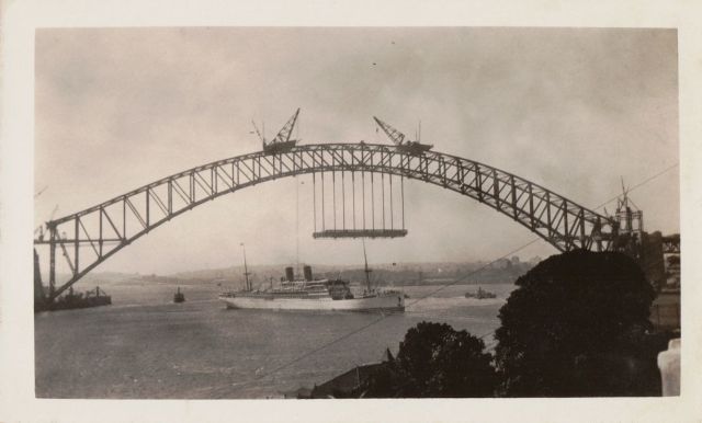 Sydney Harbour Bridge. The bridge frame has now been joined in the middle. The first stages of the deck are being built below. The deck will carry the railway line and the road for the cars. Date: probably between October and December 1930. Photo taken from McMahons Point.